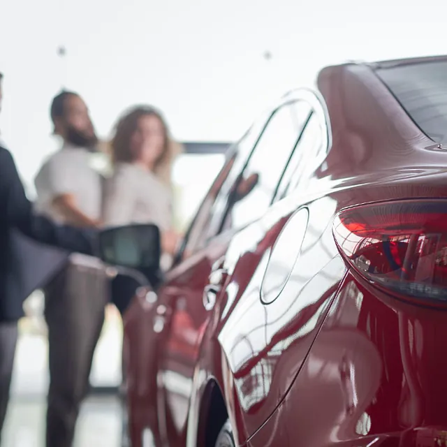 Bilde av en bil og to personer som prater med en bilselger hos en bilforhandler